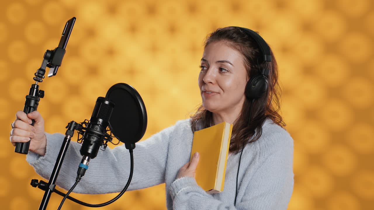 Influencer registra una recensione di un romanzo con lo smartphone e un bastone per selfie, su sfondo da studio.
