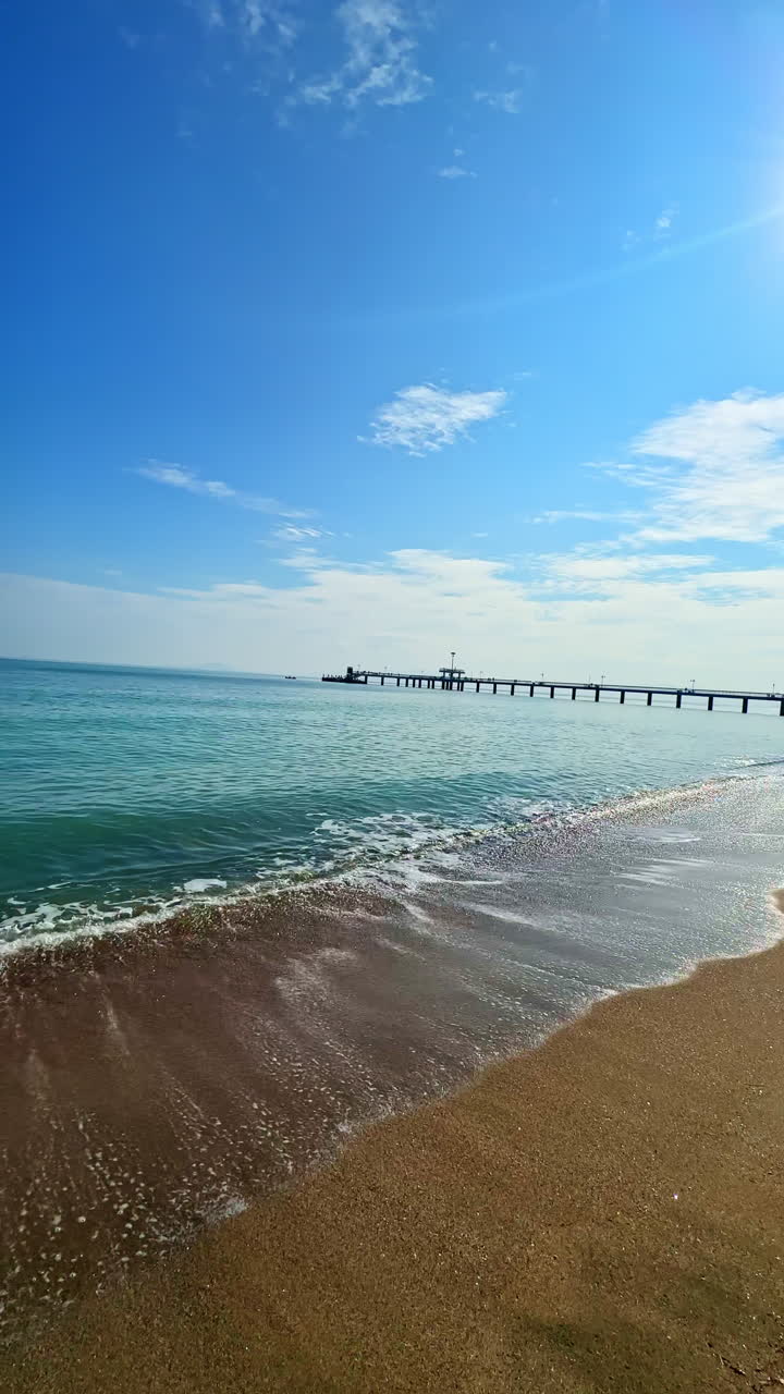 Ombak mengalir ke pantai dengan air yang tenang dan langit yang cerah di bawah cahaya sore hari