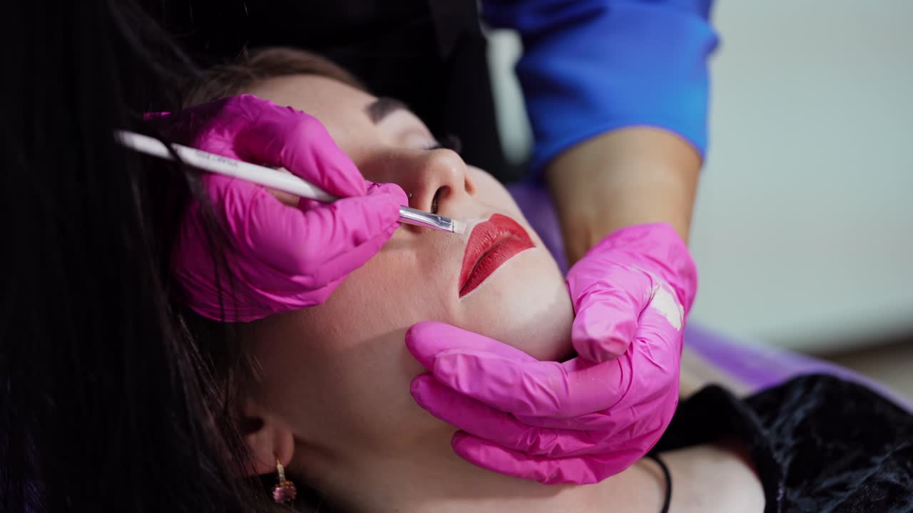 Beautician paints contour on woman's lips. Preparation before the permanent makeup on lips. Plastic medicine and cosmetology.