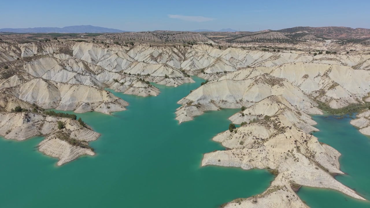 İspanya'nın Murcia bölgesinde, dramatik erozyona uğramış kötü araziler ve çöl benzeri manzaralarla çevrili Embalse de Algeciras'ın turkuaz sularının drone havadan görünümü.
