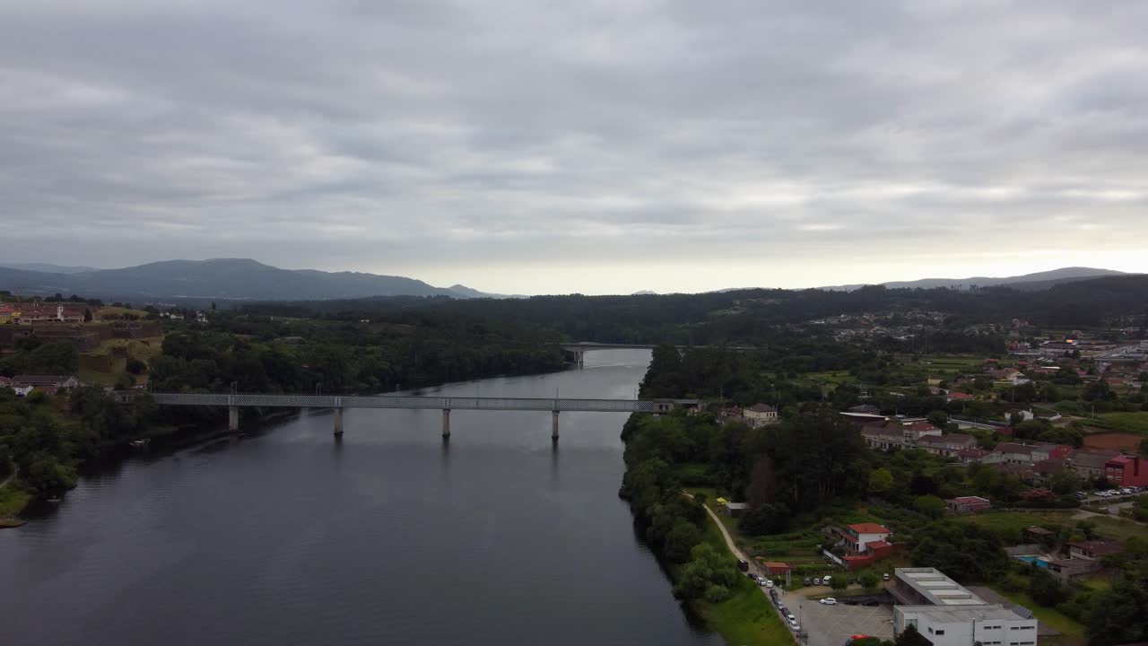 4K drone over the Minho River, showcasing the modern bridge connecting Spain and Portugal near the town of Tui, Galicia, with surrounding villages under a dramatic cloudy sky