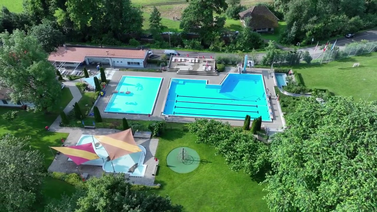 Luftfoto, der cirkler over swimmingpool og vandrutsjebane på en schweizisk feriecampingplads.