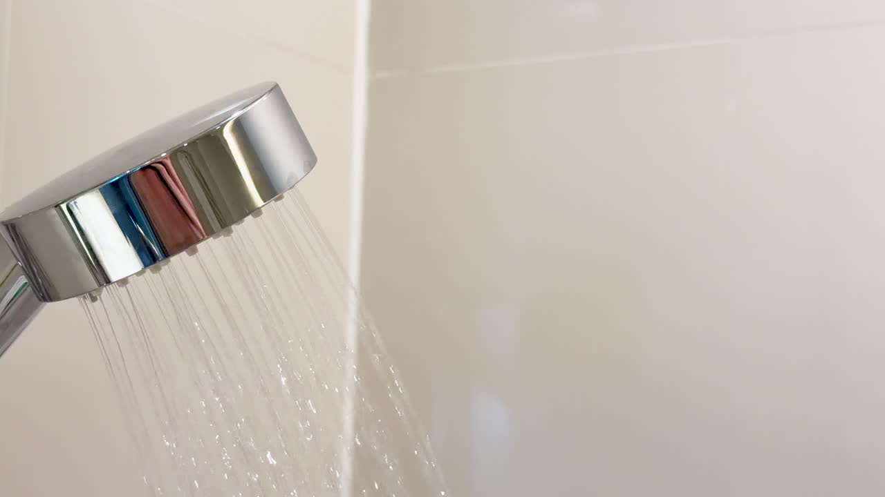 Steady stream of hot water pours from chrome shower head in bright, tiled bathroom setting
