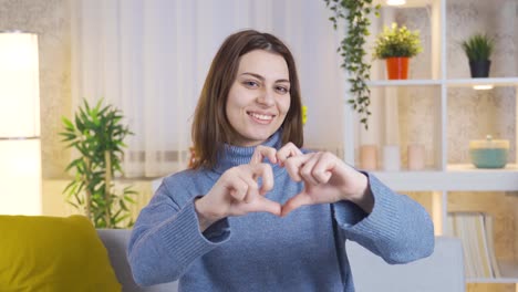 charming young woman makes heart sign looking at camera.