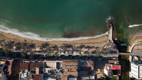 waves crashing on tropical island beach with palm trees and dramatic aerial drone reveal shot of marina and port soller mallorca spain with people walking