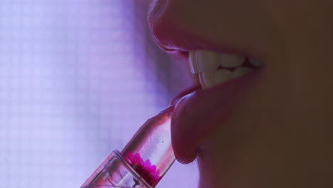 se aplica brillo de labios a sus labios mientras las luces de movimiento led brillan en el fondo