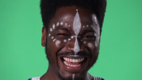 retrato de un joven afroamericano mirando a la cámara con una expresión sorprendida y entusiasta. hombre negro con un patrón blanco étnico en la cara posando en pantalla verde en el estudio.
