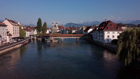 River-Reuss-in-Lucern,-entering-the-historic-city-center-with-its-many-bridges-on-an-aerial-flight