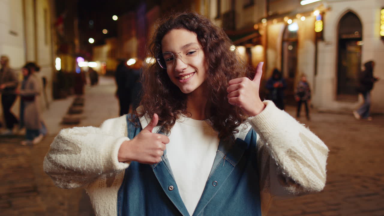 Happy teenage child looking approvingly showing thumbs up like sign positive feedback in city street