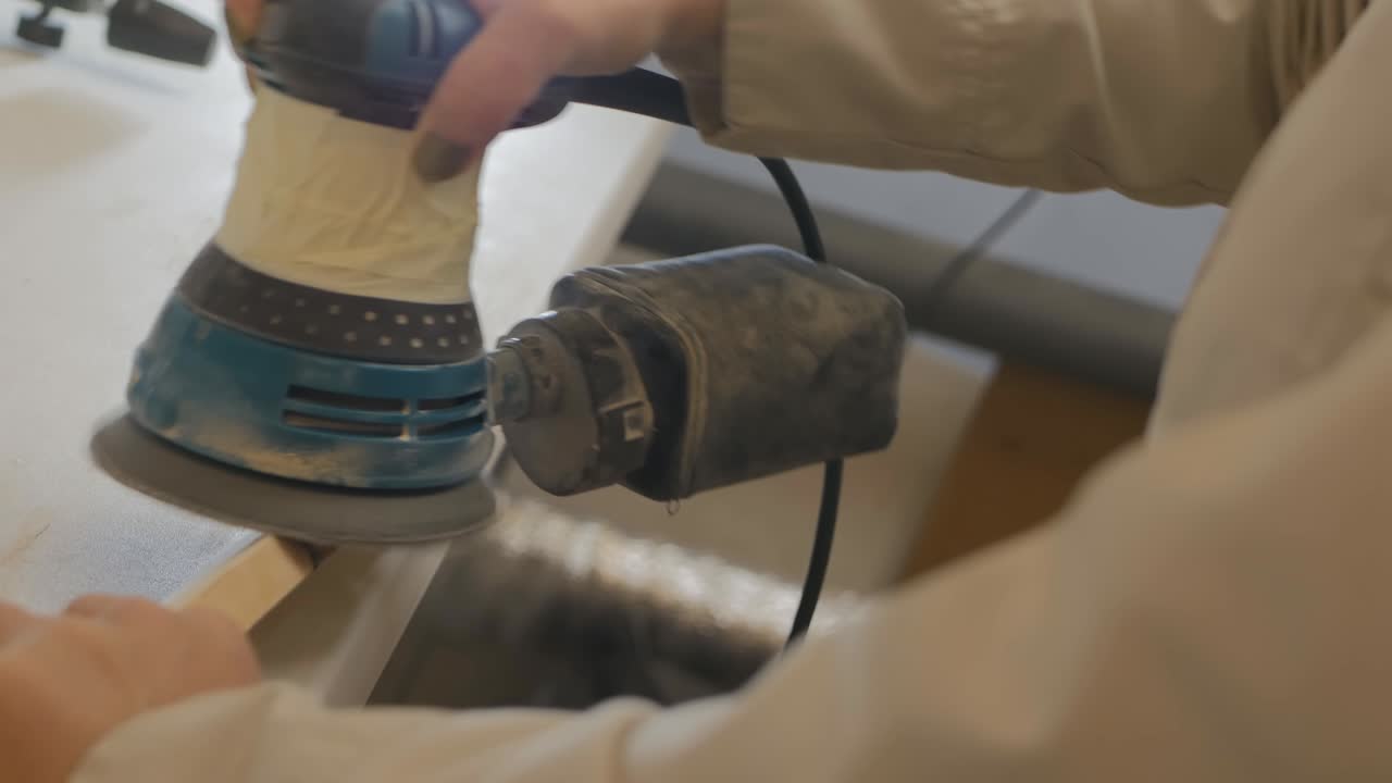joven carpintero trabaja con un molinillo. ella pulida la pieza de madera para hacerla lisa para pintar. mujer carpintero lijando la superficie. carpintería. 4k.