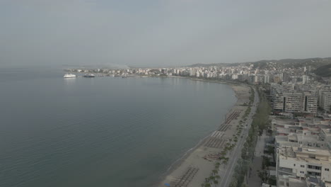 Drohnenaufnahme-über-Der-Stadt-Vlore,-Albanien,-Mit-Blick-Auf-Die-Gebäude-Und-Den-Hafen-Mit-Der-Fähre-Mit-Dem-Meer-Und-Dem-Strand-Darunter-An-Einem-Sonnigen-Tag-Mit-Etwas-Dunst