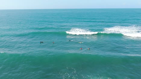 Costa-Rica-beach-drone-view-showing-sea,-surfing-people-sitting-on-their-boards