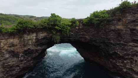 aerial ascend shot of broken beach devil's billabong with ocean and walking people in nusa penida, bali