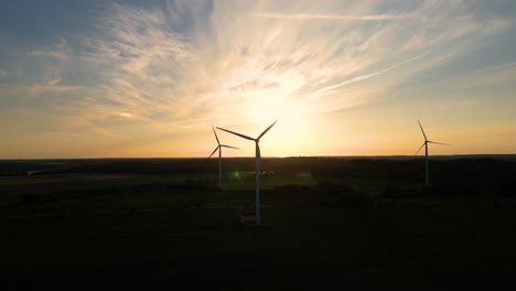 grandes turbinas eólicas con palas en el campo vista aérea puesta de sol naranja brillante cielo azul parque eólico cámara lenta giro de drones