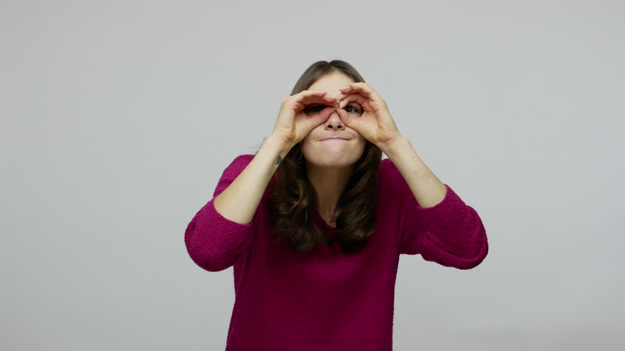 mujer morena con una sonrisa graciosa explorando el mundo a su alrededor, mirando a través de los dedos en los binoculares gesto