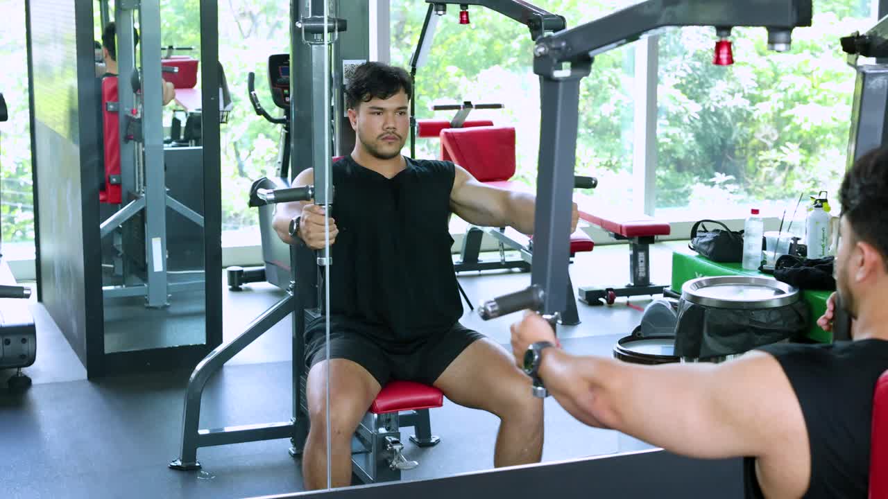 A man performs chest exercises on a machine with a trainer's guidance in a well-lit gym environment
