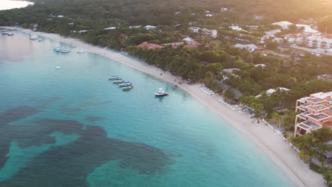 cinematic aerial view of caribbean reef with boats, turquoise water, beach, resorts at sunrise, island background, roatan island, honduras, central america