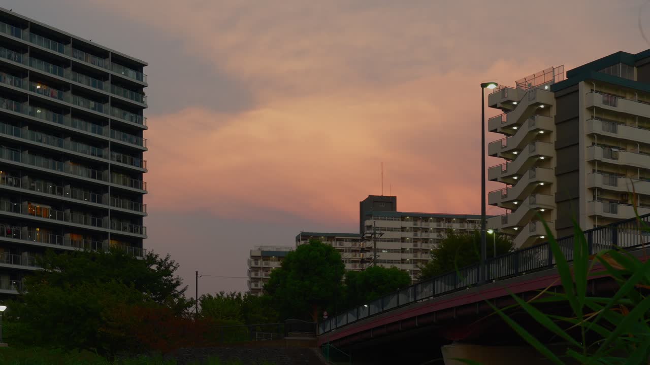 Uma vista de prédios de apartamentos e uma passarela contra um céu vibrante e nublado ao entardecer