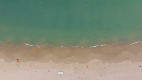 scenic drone birdseye view of sandy beach shore with blue ocean with waves and people in distance, 4k slow motion artistic