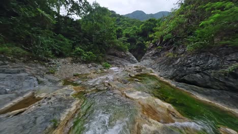 fpv drone flight over rocky river bani surrounded by vegetated nature on dominican republic