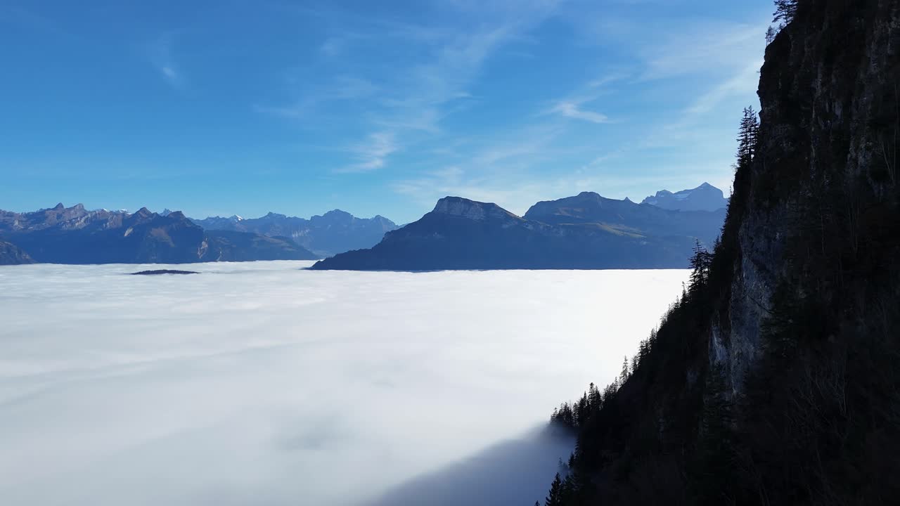 Beautiful swiss mountain landscape with layer of clouds during sunny day with blue sky. Magnificent mountain panorama in Switzerland. Conifer trees at steep slope. Wide shot.