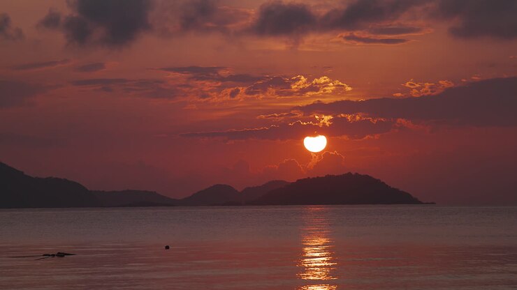 Un impresionante amanecer temprano por la mañana resplandece en rojo y naranja con nubes moradas sobre las islas y el agua ondulante del mar