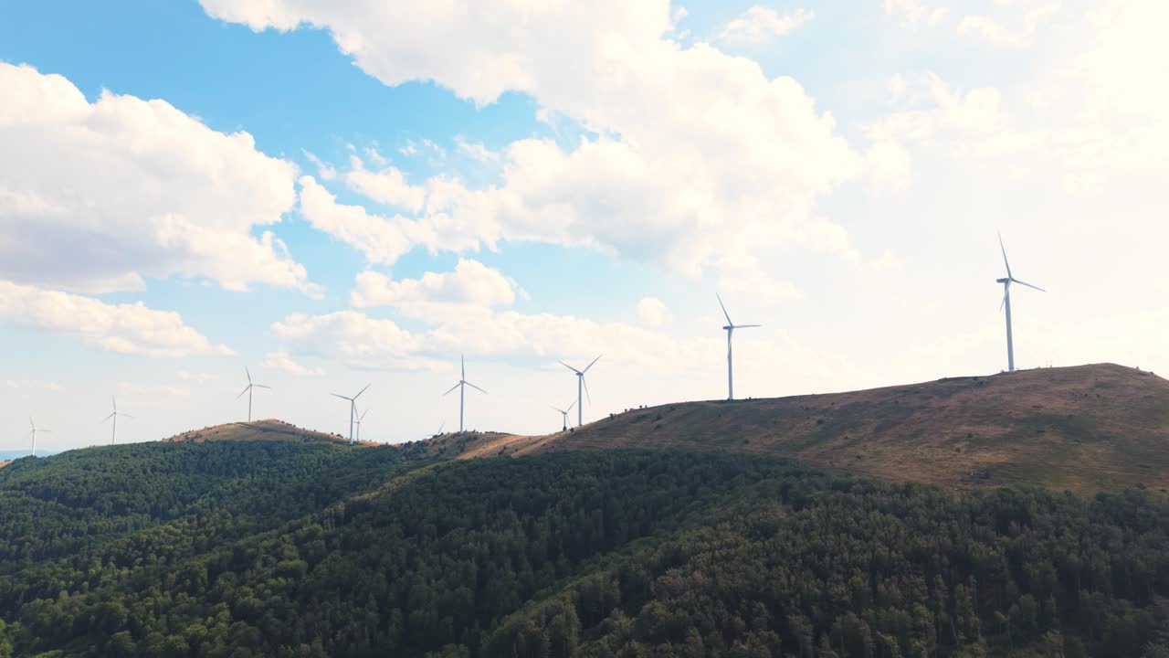 Drone view capturing the movement of renewable energy turbines under a beautiful sky. Mountains and nature offer a peaceful, sustainable backdrop