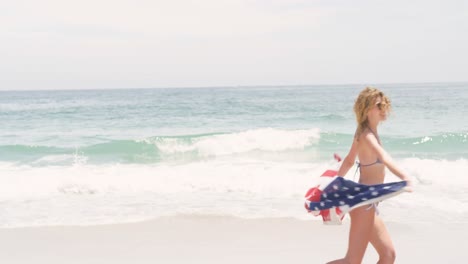 Side-view-of-Caucasian-woman-with-waving-American-flag-running-on-the-beach-4k