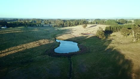 aerial footage away from the sun of a farm dam and round haybales in a field near east trentham, central victoria, australia