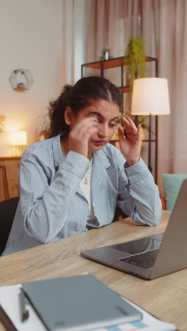 tired ill indian woman using laptop and suffering from headache problem tension sitting at table