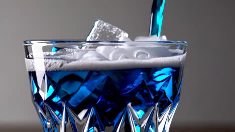 pouring blue cocktail into a glass with ice