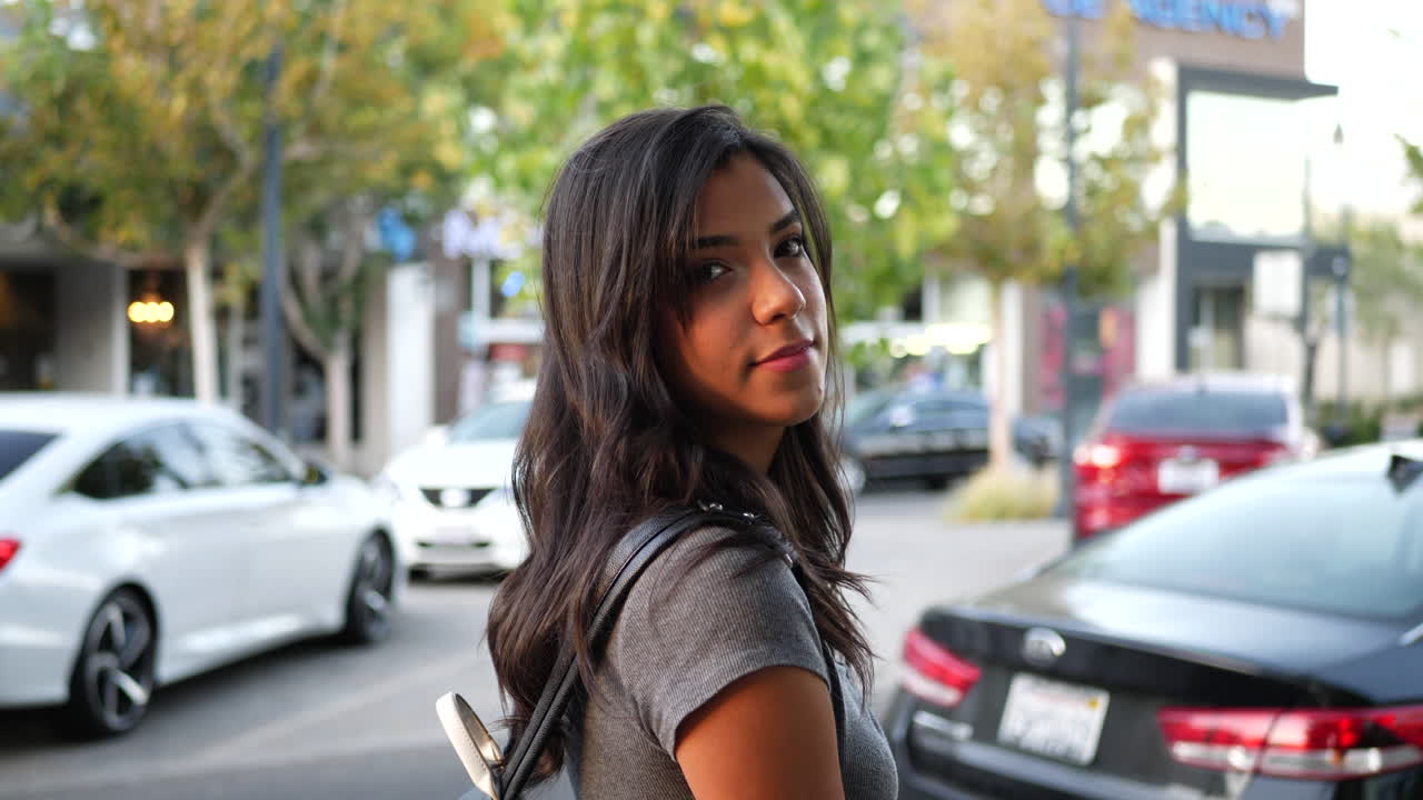 una hermosa joven hispana caminando por la calle de la ciudad mirando en las ventanas de la tienda mientras compra en cámara lenta al atardecer