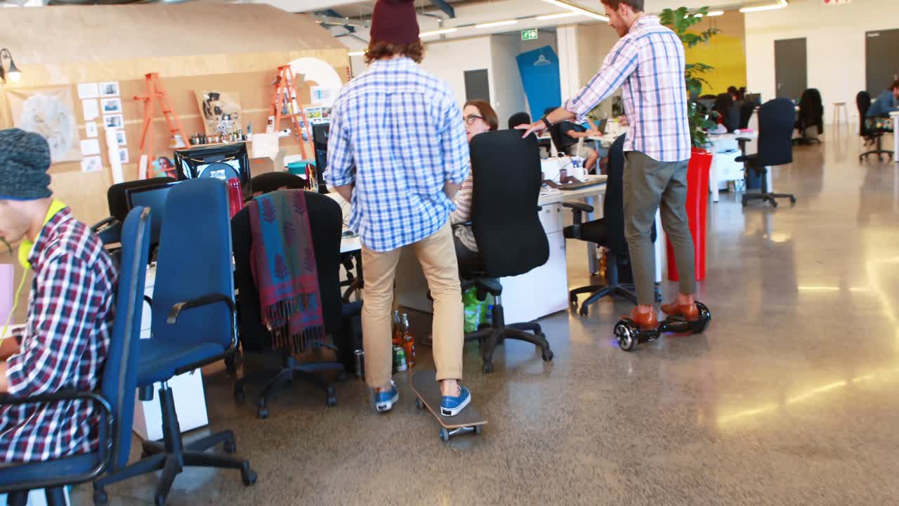 Two businessmen using hoverboard and skateboard while coworkers working
