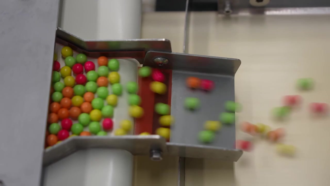 Colorful round pellets sliding through a stainless vibrating feeder chute