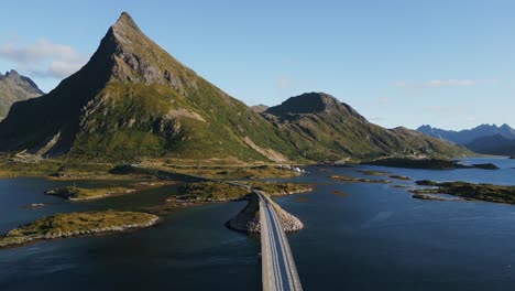 siguiendo un coche que pasa por el solitario puente fredvang road en lofoten norte de europa con vista hacia el solitario pico de la montaña entre verano y otoño