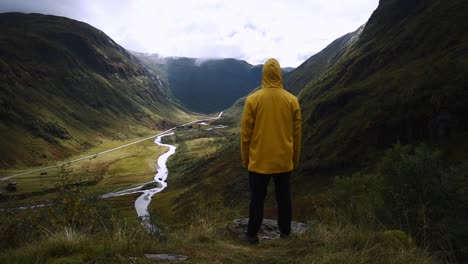Hombre-Con-Chaqueta-Amarilla-Disfrutando-Del-Impresionante-Paisaje-Montañoso-De-Un-Valle-En-Noruega