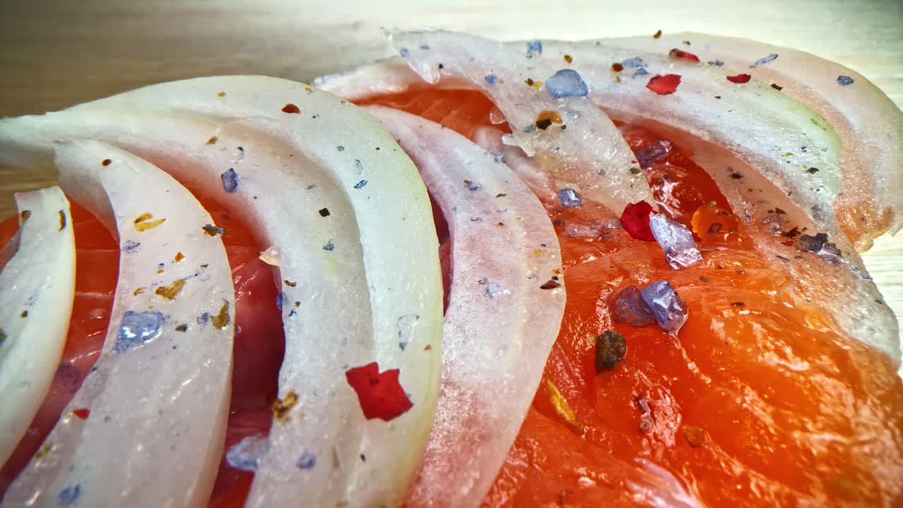 Closeup of salt grains falling on Thin onion slices on salmon slices on cutting board
