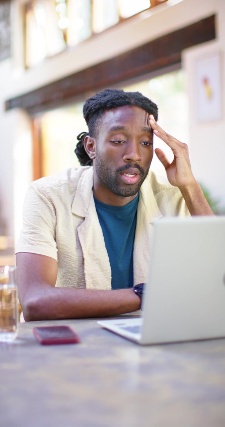Vertical video: African American man leaning at table, reacting to laptop message and gesturing