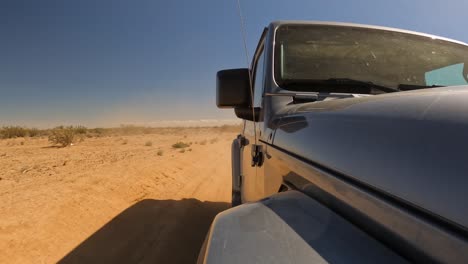 a shiny new off-road vehicle driving through the dust and dirt of the mojave desert - front of the jeep looking back