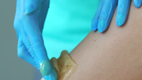 Close-up-in-the-beauty-salon-master-in-gloves-doing-the-procedure-to-remove-the-hair-on-the-legs-with-a-sugar-mixture