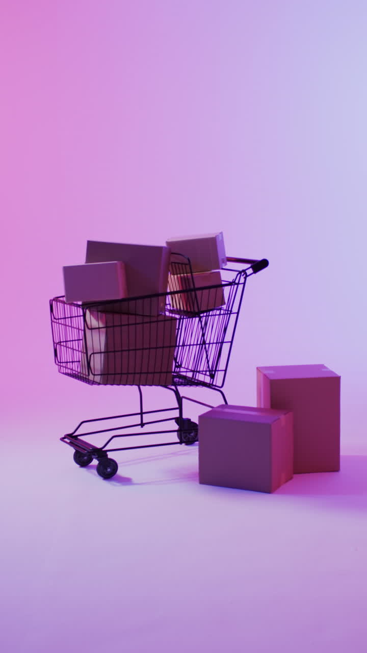 Vertical video of shopping trolley and boxes with copy space over pink neon background