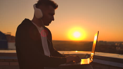 rear view of a man in headphones listening to music and working on the roof of a building at sunset with a view of the city from a height. roof of a skyscraper at sunset.