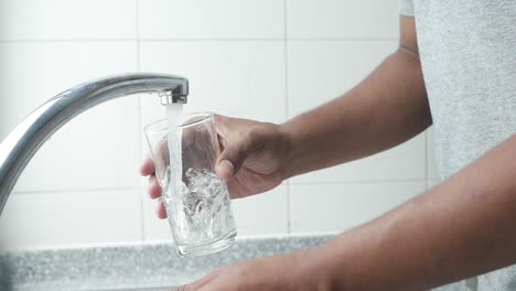 person filling glass of water from tap