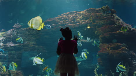 young girl at aquarium watching fish swimming in tank curious child having fun looking at colorful marine life in oceanarium aquatic habitat