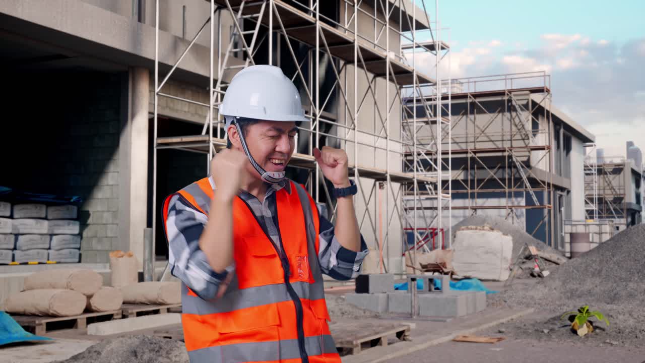 Asian Male Engineer With Safety Helmet Screaming Goal And Dancing Celebrating At Building & Construction Site in Progress to New House