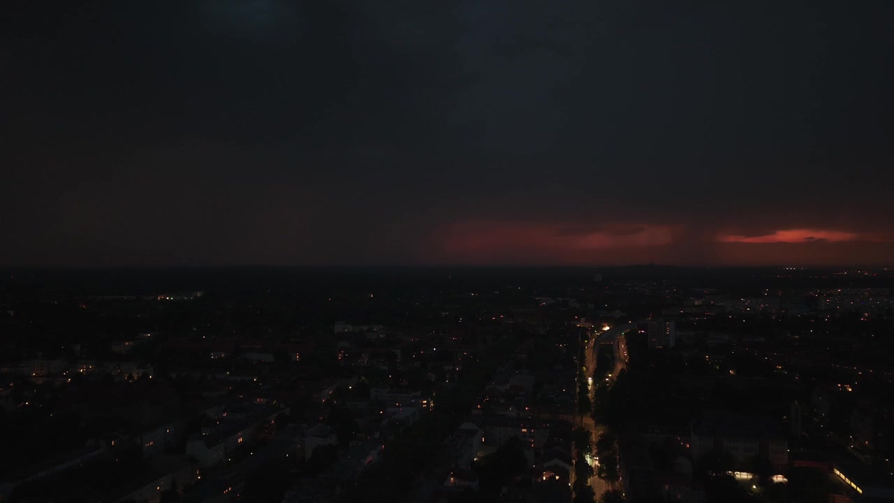 Blesky šlehající nad městem v noci, osvětlující mraky a panorama města s auty jedoucími po ulici během bouřky. Úžasný letecký pohled klesajícího dronu panoráma