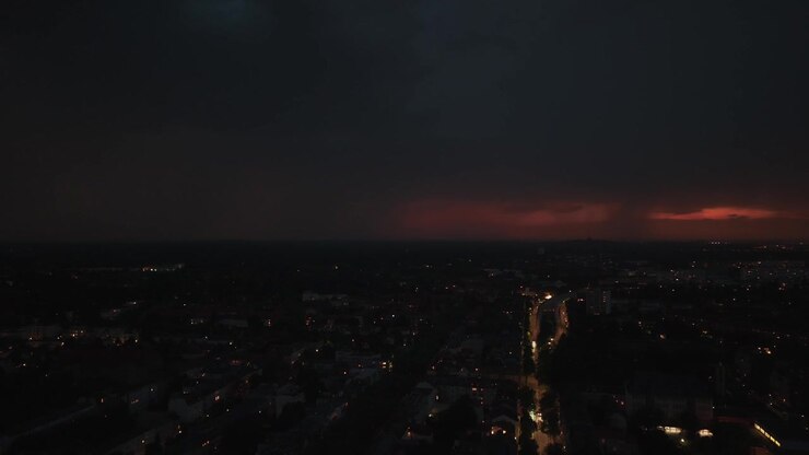 Fulmini che illuminano una città di notte, rischiarando nuvole e skyline con auto che guidano su una strada durante un temporale. Favolosa vista aerea panoramica con drone in discesa.