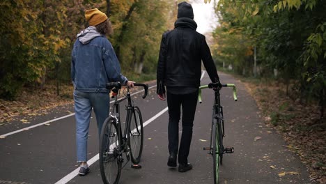 Two-Close-Friends-Having-Lovely-Walk-With-Bikes-In-City-Park-Between-Green-And-Yellow-Tall-Trees,-Concept-Of-Active-Lifestyle,-Communication,-Dating