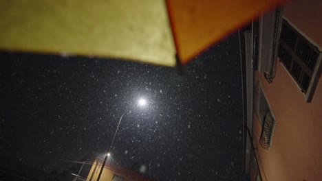 movimiento lento estático durante una nevada en una ciudad por la noche apuntando a una lámpara de calle desde un paraguas