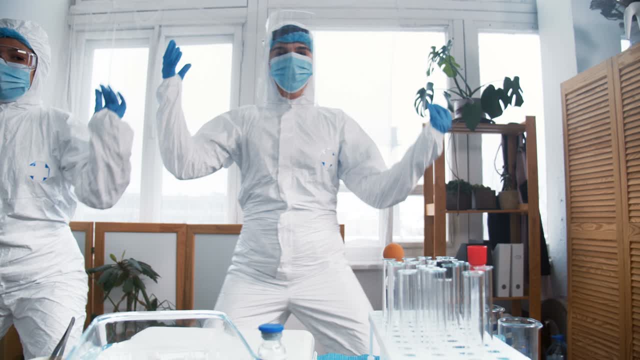 Celebrating success. Two excited crazy happy female chemical lab doctors in white protection suits do fun dance at work.